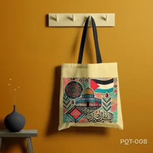 Noor al Aqsa Tote Bag (PQT-008), a light cream canvas tote, featuring a vibrant, intricate illustrative design of the Dome of the Rock (Al-Aqsa compound), the Palestinian flag, Arabic calligraphy, and floral/geometric motifs in red, blue, green, gold, and black, with black handles, hanging from a light wooden peg rack against a deep golden-yellow wall, with a dark grey vase on a small black table to the left.