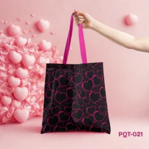Love Pulse Tote Bag (PQT-021), a black canvas tote, featuring a repeating pattern of black heart silhouettes outlined in vibrant magenta/pink, with matching magenta/pink handles, held by a hand and displayed upright on a pink surface against a pink wall adorned with decorative pink hearts and textured elements.