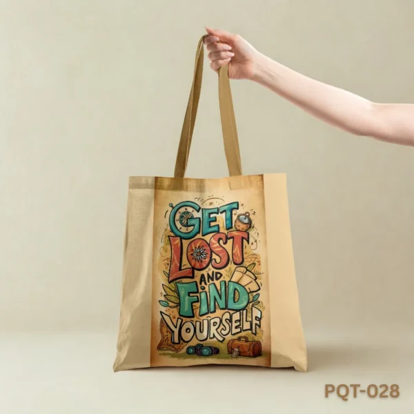 Adventure Boldly Tote Bag (PQT-028), a light beige canvas tote, featuring a central panel with a colorful, illustrative typographic design "GET LOST AND FIND YOURSELF" surrounded by travel-themed doodles like a compass, map, and luggage, held by a hand against a plain light beige background.