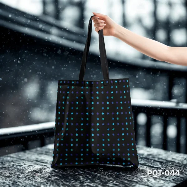 Stellar Stride Tote Bag (PQT-004) featuring a vibrant, ornate paisley pattern in teal, pink, orange, and white on a dark navy blue background, with black handles, displayed upright on a rustic dark wooden shelf against a mottled grey textured wall, with dried flowers in terracotta vases.