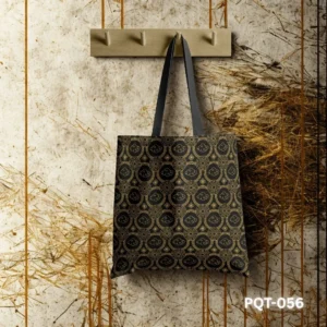 Celestial Echoes Tote Bag (PQT-056) featuring an elegant traditional Asian-inspired geometric pattern with cloud motifs in gold on a black background, with black handles, hanging from a light wooden peg rack against a textured beige and brown wall with dried grass accents.