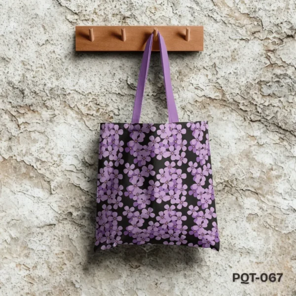 Lavender Garden Tote Bag (PQT-067) featuring an all-over print of small lavender purple flowers with yellow centers on a black background, with matching lavender purple handles, hanging from a light wooden peg rack against a textured, flaky beige and grey stone wall.