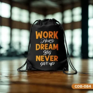 "The Unstoppable Drawstring Bag (CDB-084) in black with orange and white motivational text 'WORK HARD DREAM BIG NEVER GIVE UP,' shown on a polished wooden floor with a blurred gym or studio background."