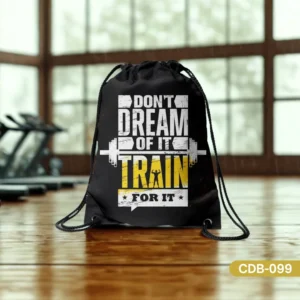 Black Dream Achiever Drive Drawstring Bag (CDB-099) with "Don't Dream Of It Train For It" motivational quote, displayed on a wooden floor in a gym setting.