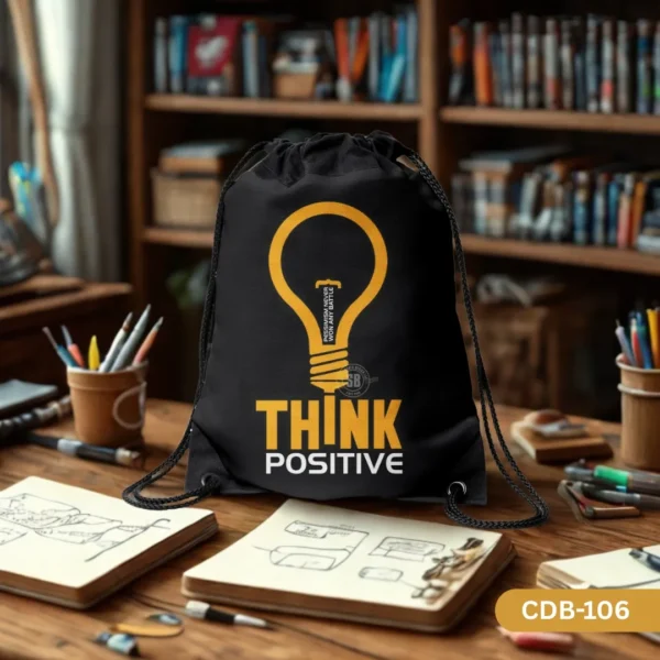 "Positive Filament black drawstring bag with a yellow lightbulb design and 'Think Positive' text, resting on a wooden desk with notebooks and study supplies."