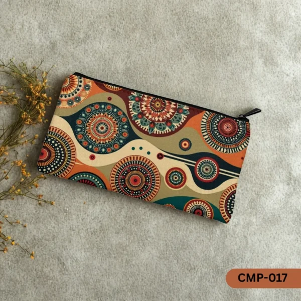 "CMP-017 Mosaic Magic Makeup Pouch with an intricate pattern of earthy-toned mosaic circles, displayed on a textured grey surface next to a sprig of dried yellow flowers."
