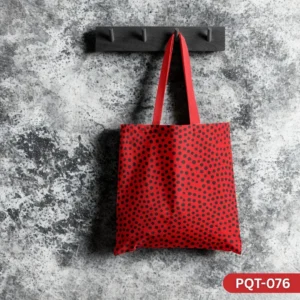 Urban Dotscape Tote Bag (PQT-076) featuring a vibrant red background with an all-over pattern of small black polka dots, with matching red handles, hanging from a dark wooden peg rack against a textured, distressed grey concrete wall.