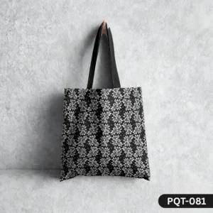 Botanic Noir Tote Bag (PQT-081) featuring a dense repeating pattern of stylized white and grey flowers on a black background, with black handles, hanging from a single light-colored peg against a textured white wall with a subtle floral imprint.
