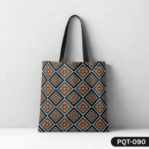 Tribal Trend Tote Bag (PQT-090) featuring a repeating geometric diamond and tile pattern in black, white, red, and yellow, with black handles, displayed upright on a white surface against a light grey textured wall.