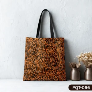 Zebra Noir Tote Bag (PQT-096) featuring a vibrant orange and black stylized zebra stripe print with black handles, displayed upright on a white wooden surface against a textured white wall, with two copper-colored vases containing dried flowers to the right.