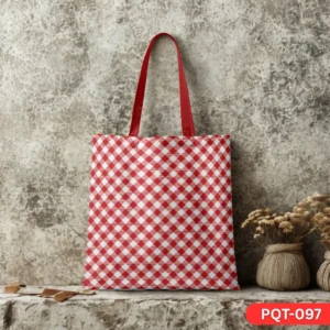 Vintage Vibe Tote Bag (PQT-097) featuring a classic red and white diagonal gingham checkered print with red handles, displayed upright on a rustic stone ledge against a textured mottled grey wall, with small rustic vases of dried flowers to the right.