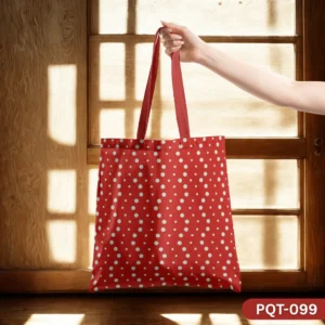 Dotella Charm Tote Bag (PQT-099) featuring a vibrant red background with a playful white polka dot pattern and red handles, held by a hand in front of a sunlit wooden window frame and wall.