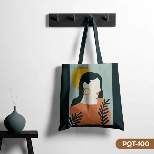 Helia Grace Tote Bag (PQT-100) featuring a modern illustrative design of a faceless woman with dark hair and a gold hoop earring, set against a yellow sun and botanical elements on a light blue-green panel, with dark green side panels and handles, hanging from a dark grey peg rack against a white wall, with a dark teal vase on a small black table to the left.