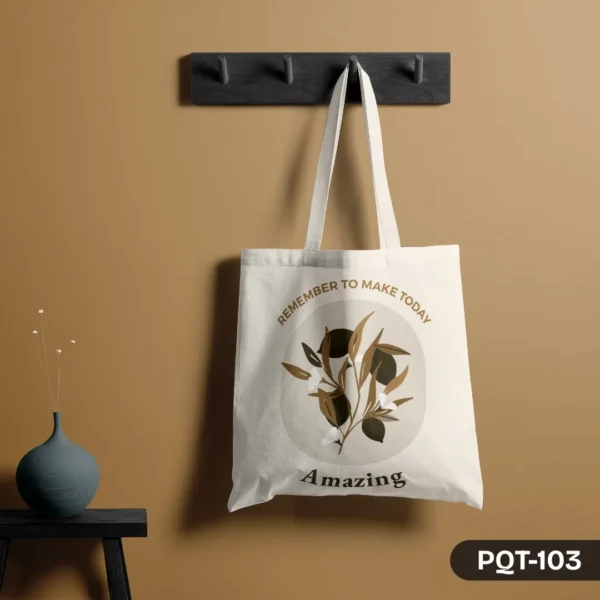 Inspire Grace Tote Bag (PQT-103), a white canvas tote featuring an elegant olive branch design in a central circle with the inspirational quote "Remember to make today Amazing," hanging from a dark grey peg rack against a warm tan wall, with a teal vase on a small black table to the left.