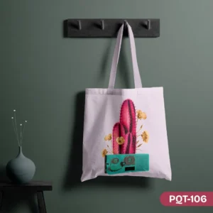 Cactus Groove Tote Bag (PQT-106), a white canvas tote, featuring a vibrant pink cactus with yellow flowers emerging from a retro teal radio/cassette player design, hanging from a dark grey peg rack against a dark teal wall, with a teal vase and dried flowers on a small black table to the left.
