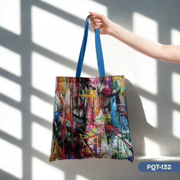 Hand confidently holding the electrifying Afterlight Tote Bag (PQT-132), showcasing its vibrant abstract graffiti art print and cool blue straps, set against a modern white wall with artistic window shadows