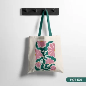Petalblock Tote Bag (PQT-134) showcasing a modern graphic floral print in pink and teal on a cream background with teal straps, hanging on a dark wood peg rail against a white wall