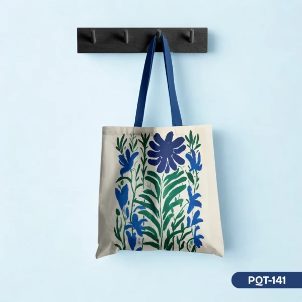 Lapis Garden Floral Tote Bag (PQT-141) showcasing a rich blue and green stylized botanical print on a light canvas with deep blue straps, hanging on a dark wood peg rail against a light blue wall.