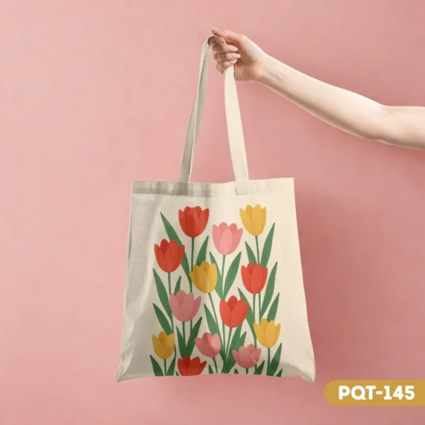 Floral Delight Tote Bag (PQT-145) with a vibrant print of red, pink, and yellow tulips, held by a hand against a soft pink background.