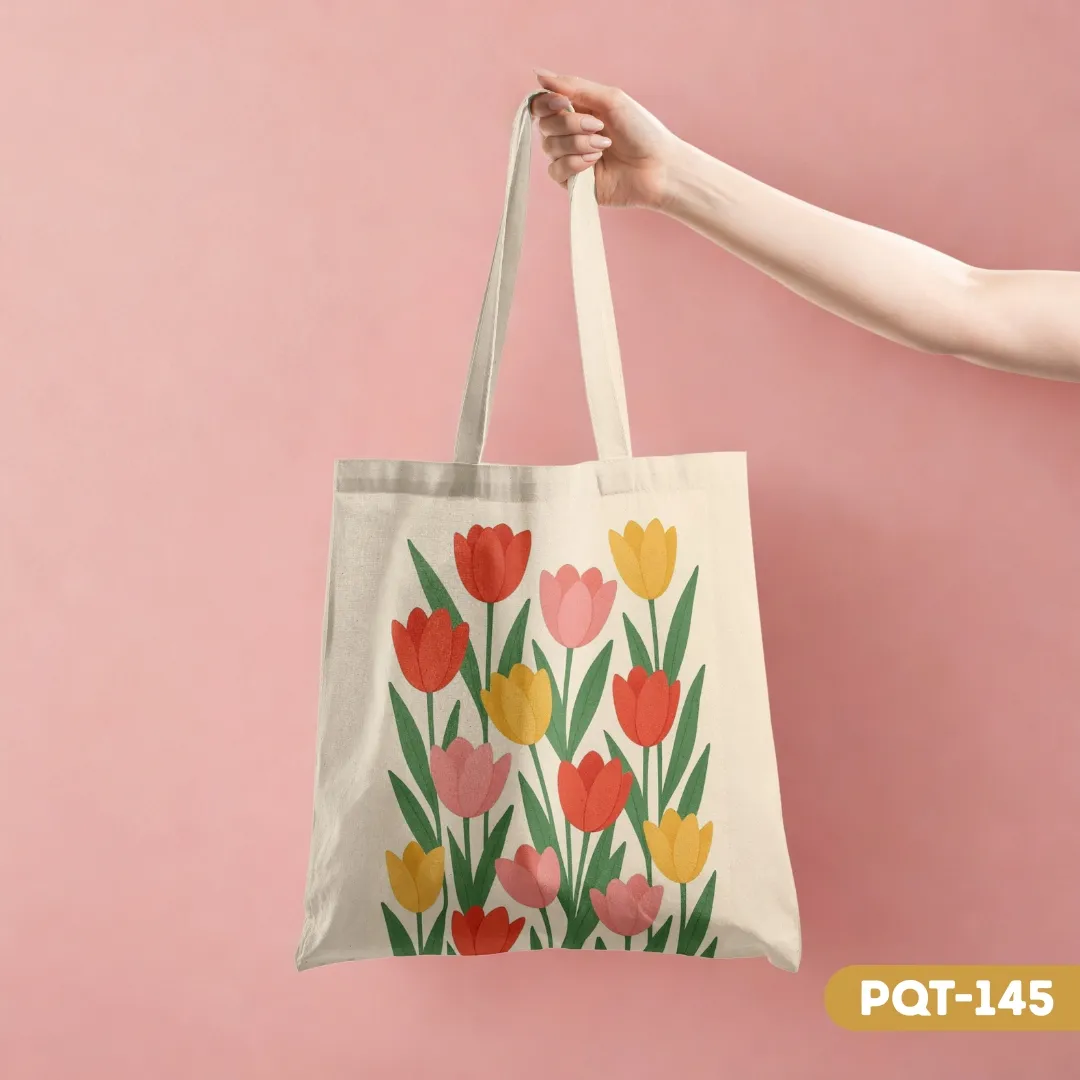 Floral Delight Tote Bag (PQT-145) with a vibrant print of red, pink, and yellow tulips, held by a hand against a soft pink background.